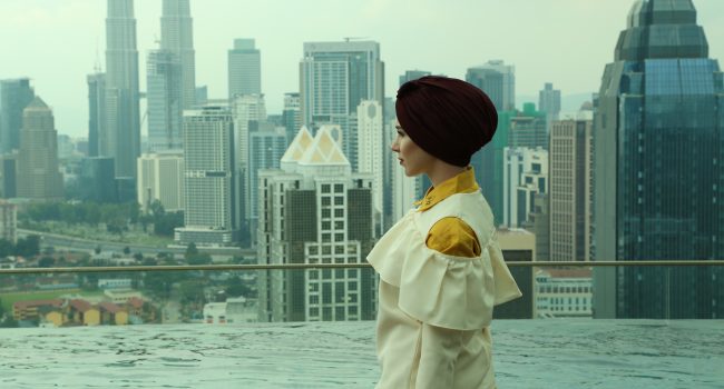 A woman in an outfit created by the "modest fashion" designer Nabiilabee stands in front of an urban city skyline. (Photo © Nabiilabee, used with permission.)